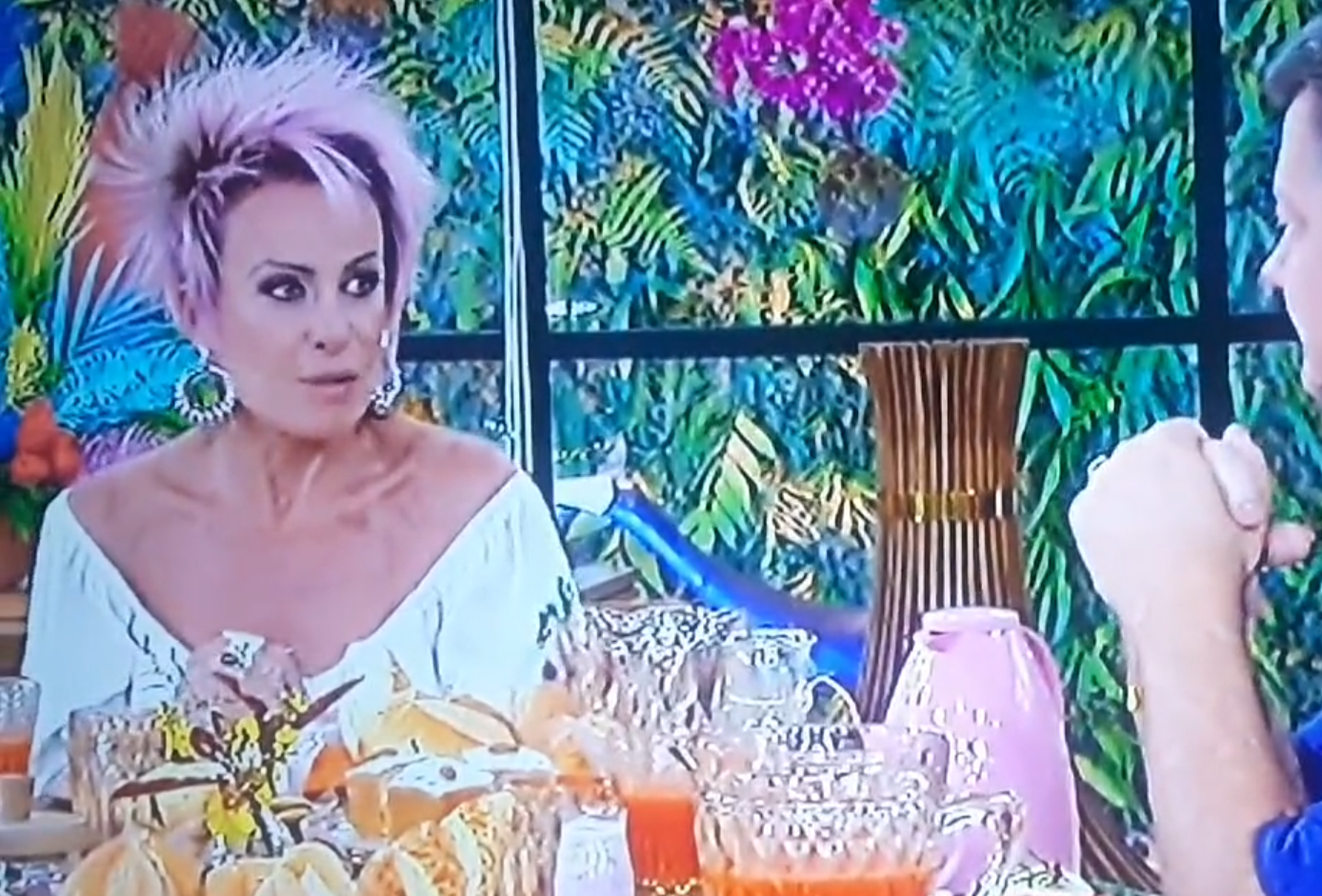 Ana Maria Braga sentada à mesa do seu programa, com o café da manhã colocado, conversando com o jornalista Renato Peters.