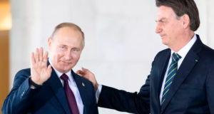 Presidente Russo, Vladimir Putin ascena em direção as câmeras e Bolsonaro toca em seu ombro