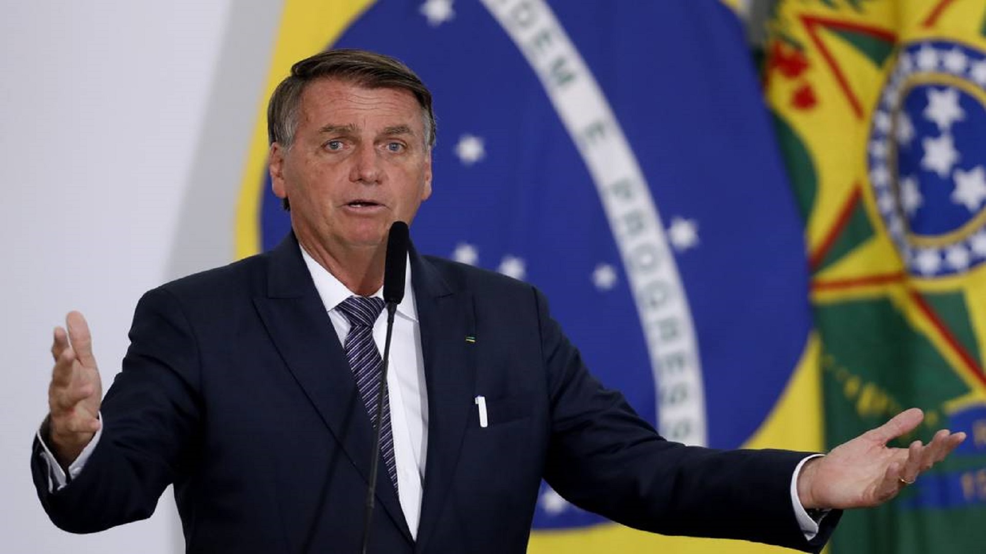 Bolsonaro discursando com os braços abertos.