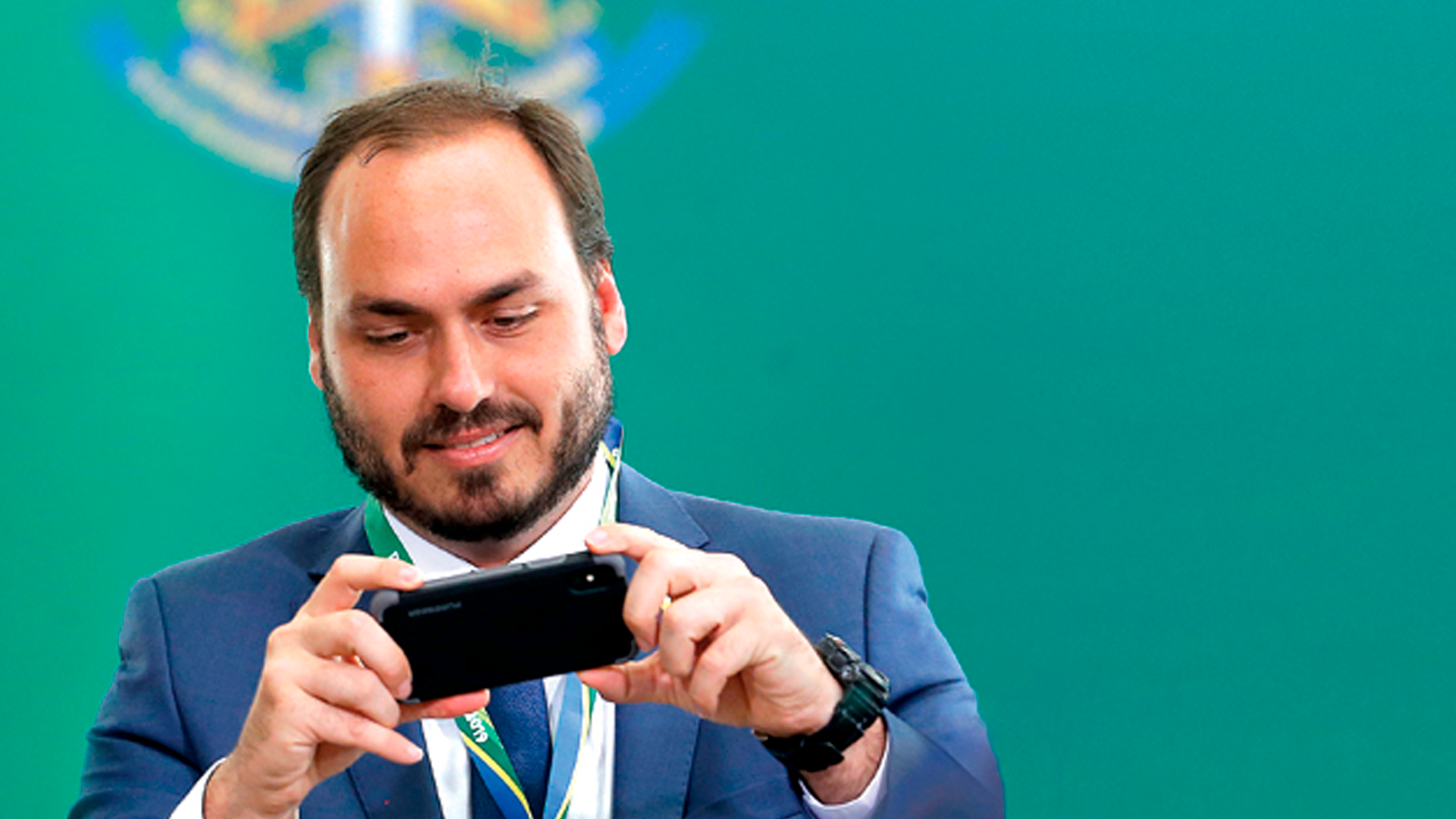 Carlos Bolsonaro sorri enquanto olha seu celular