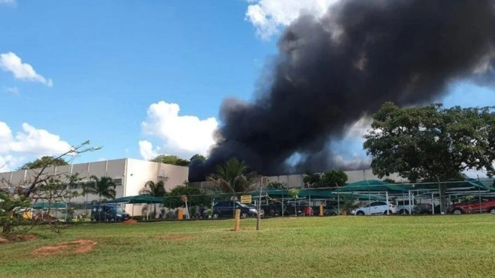 Garagem do Palácio do Planalto pega fogo. Foto de fumaça preta subindo no céu com estrutura do galpão ao fundo.