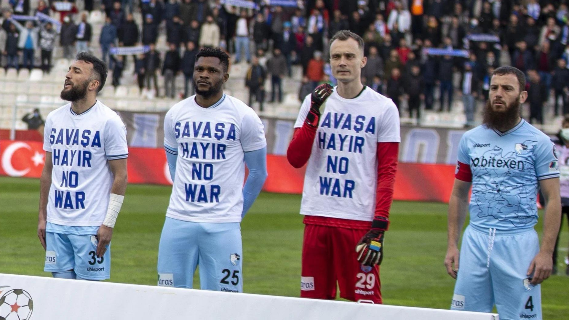 Jogador se recusa a vestir camisa contra guerra na Ucrânia. Na foto, jogadores estão um ao lado do outro vestindo uma camisa contrária à guerra na Ucrânia, excete Aykut Demir, que veste a camisa do time.