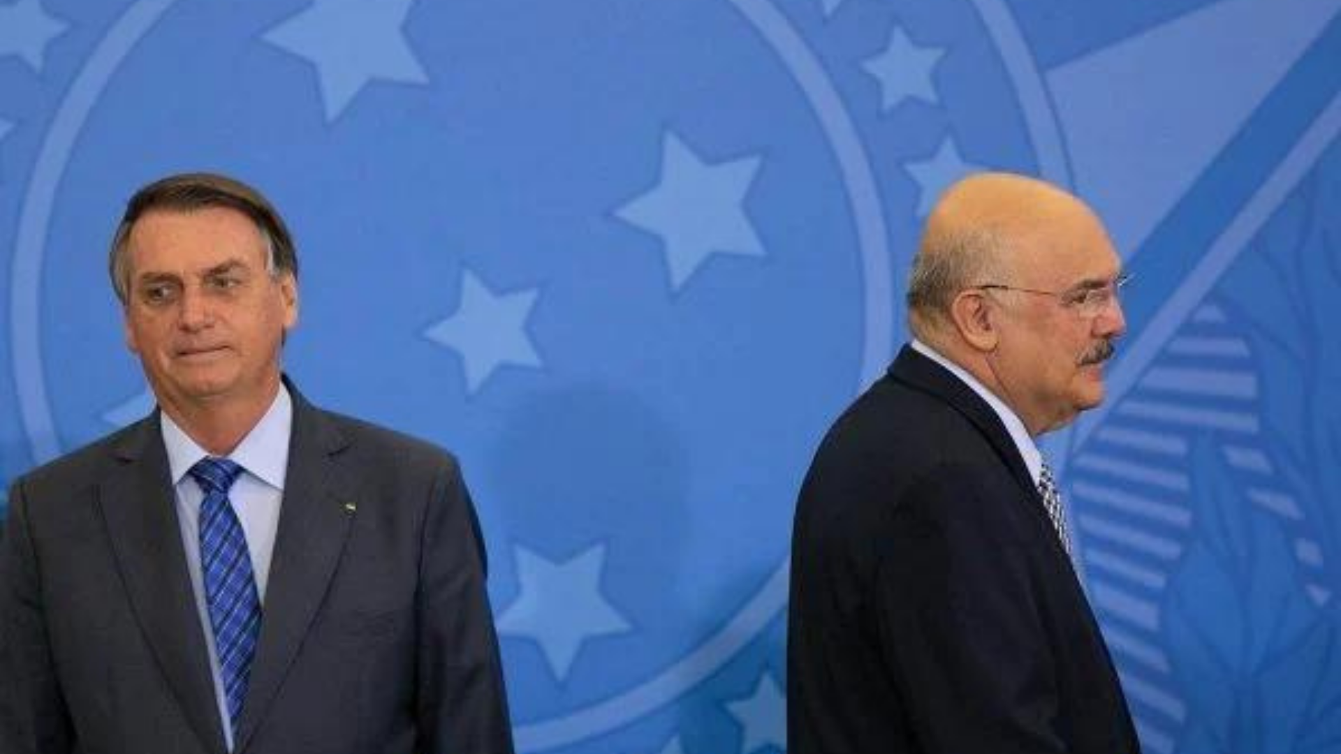 Internação de Bolsonaro ajuda a ofuscar crise no governo. Foto de Bolsonaro com olhar desconcertado e o ministro Milton Ribeiro de costas para ele. 