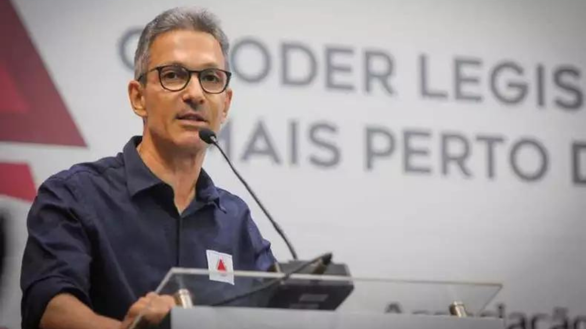 Zema ignora greve e decide não atender reivindicações de servidores. Foto do governador com camisa azul marinho, falando em um púlpito, com óculos de grau e cabelo grisalho liso