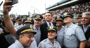 Bolsonaro quer aprovar projeto para reduzir punições a policiais. Foto do residente sorrindo rodeado de policiais posando para uma selfie na rua.