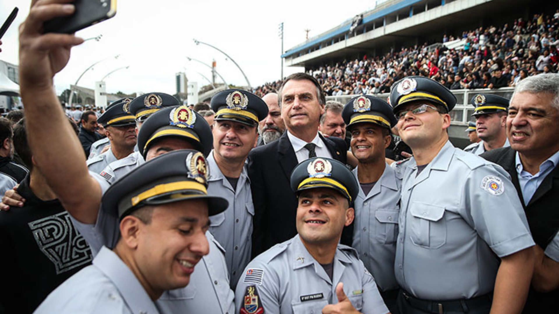 Bolsonaro quer aprovar projeto para reduzir punições a policiais. Foto do residente sorrindo rodeado de policiais posando para uma selfie na rua. 