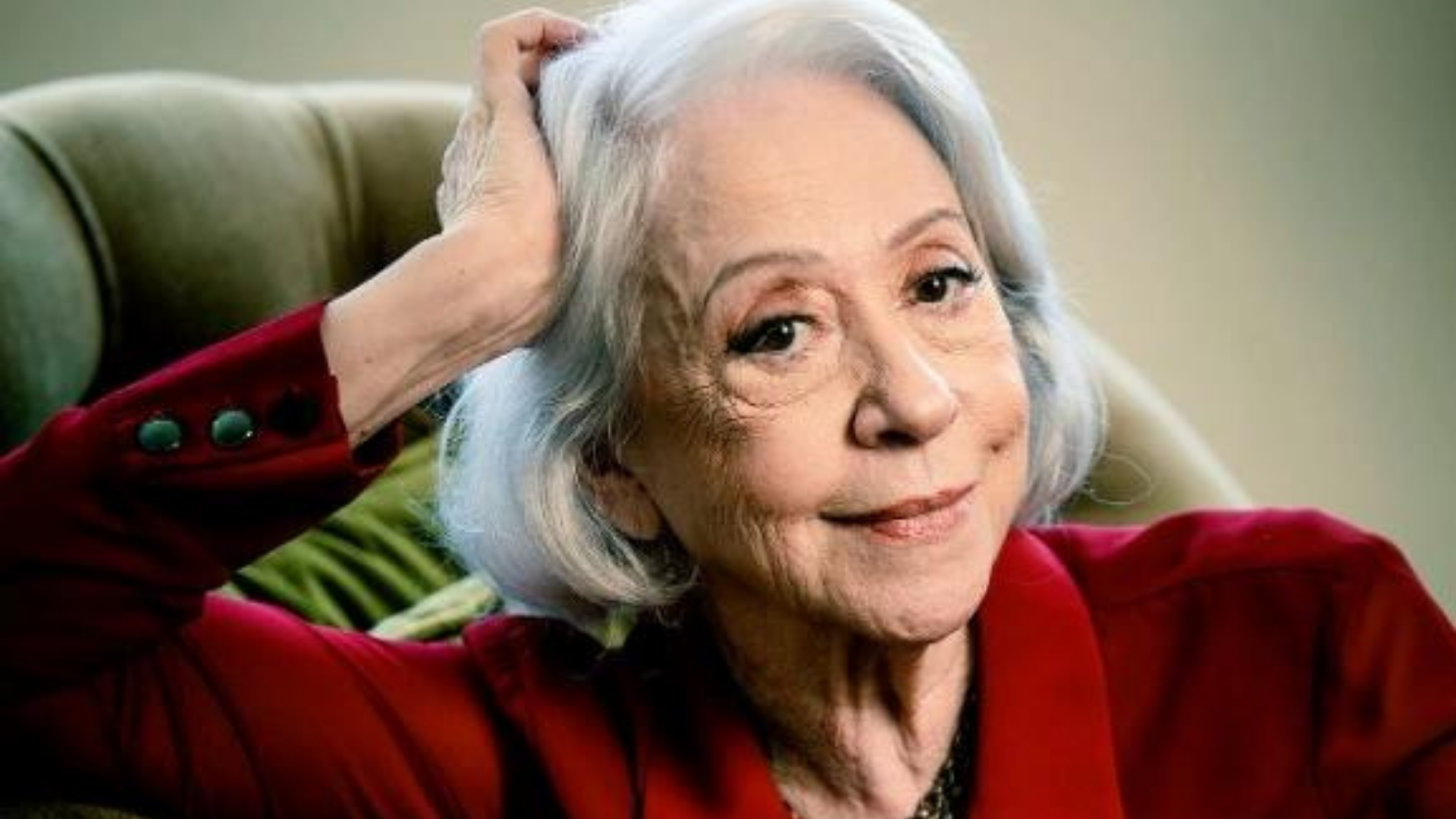 Fernanda Montenegro assume cadeira na Academia Brasileira de Letras. Foto de Fernanda Montenegro sorrindo, com batom vermelho, em um sofá.