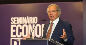 Paulo Guedes diz que Paraguai é "o estado brasileiro mais rico" e recebe bronca de ministro. Ele usa terno preto e fala em um púlpito, sem máscara.