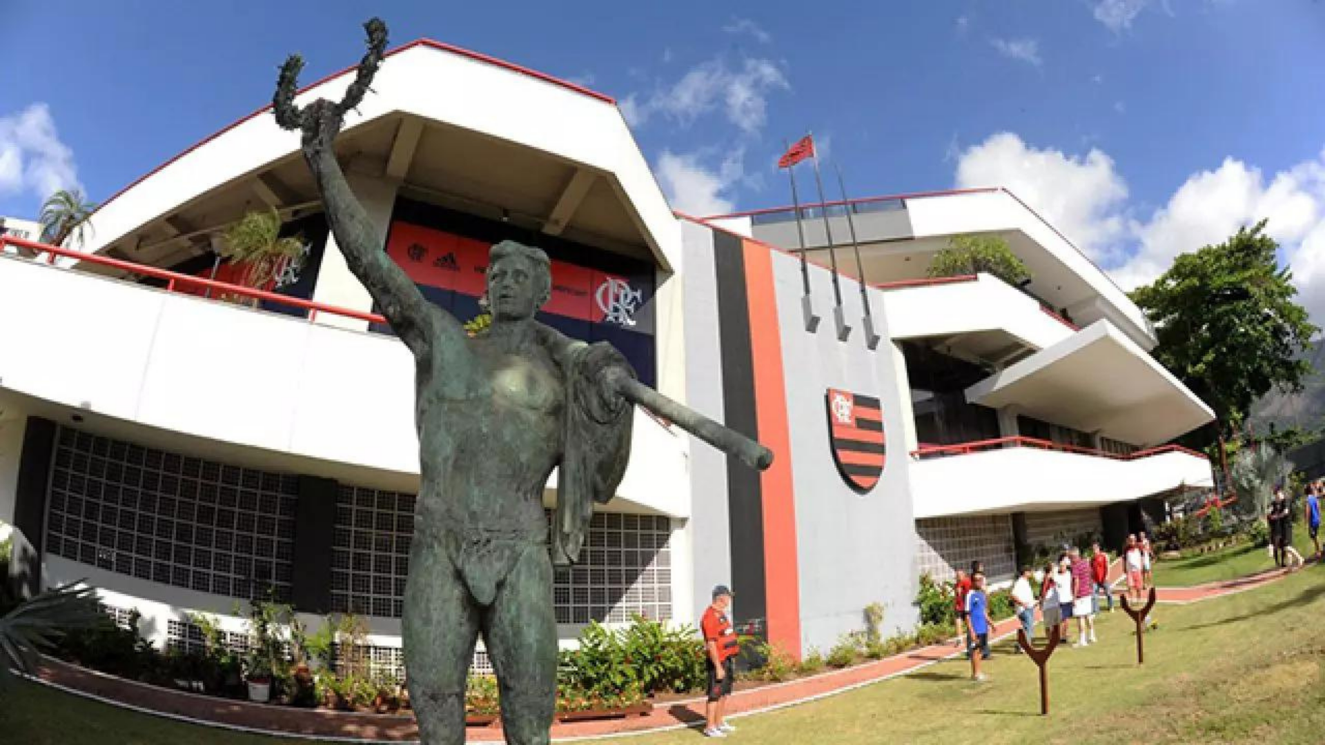 Homem tenta estuprar criança de 10 anos em vestiário do Flamengo. Foto da entrada do Clube, um prédio com arquitetura contemporânea, símbolo do Flamengo e uma estátua ao lado de fora.