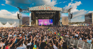 Empresa que organiza Lollapalooza recorre na justiça após censura do TSE. Foto da vista de um palco do festival com os participantes levantando as mãos para cima.