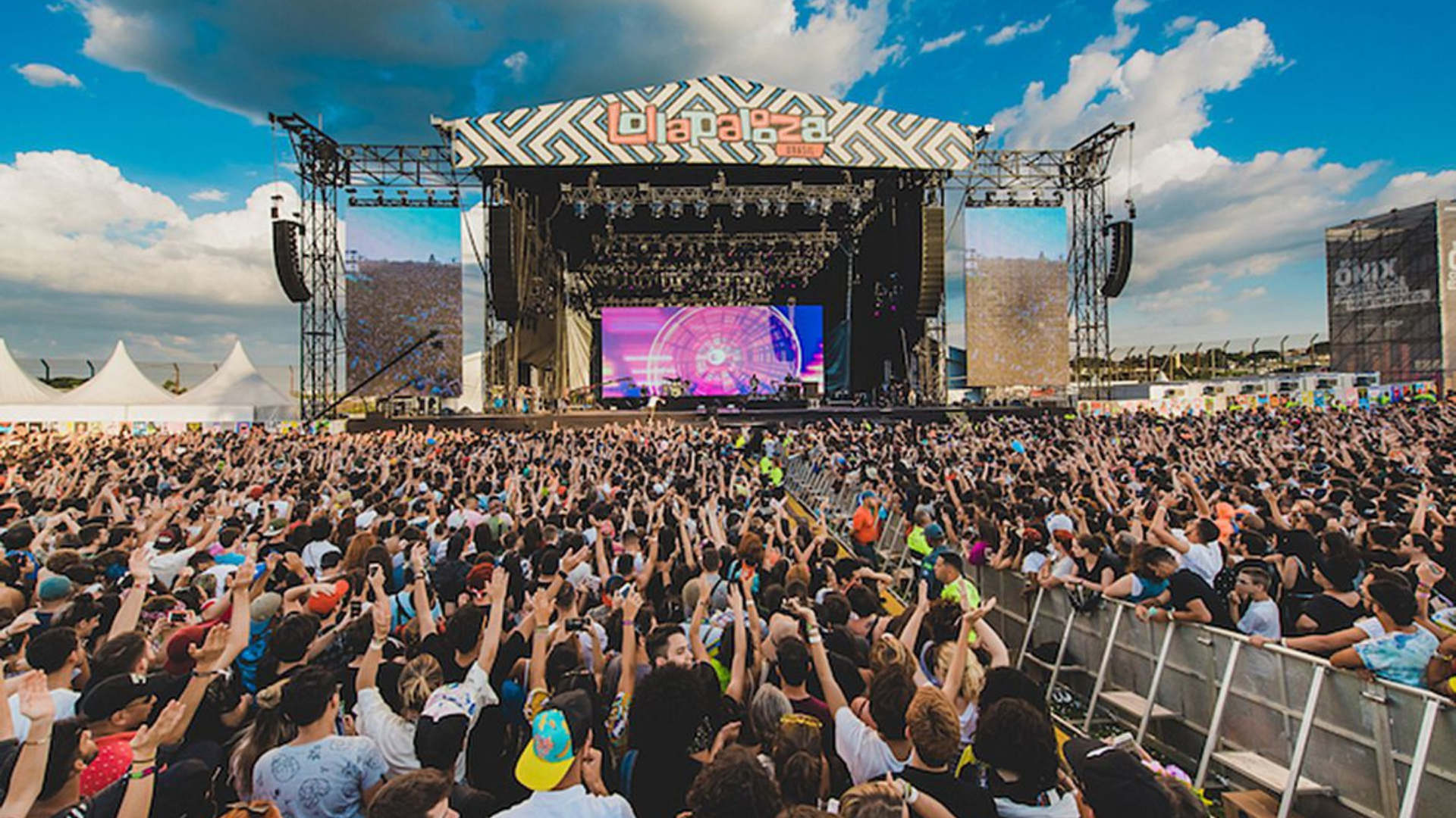 Empresa que organiza Lollapalooza recorre na justiça após censura do TSE. Foto da vista de um palco do festival com os participantes levantando as mãos para cima.