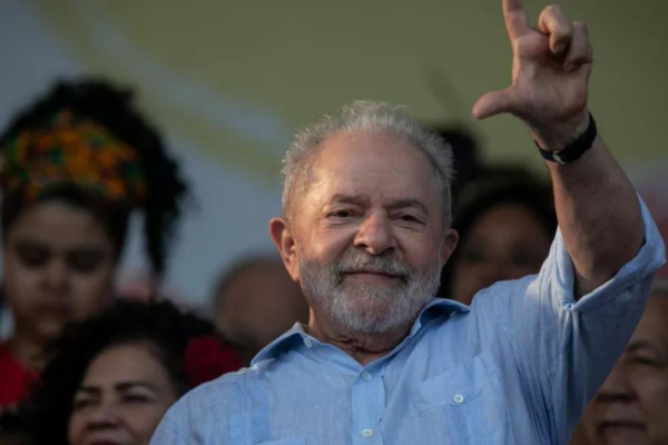 Foto de Lula fazendo o sinal de L com a mão e sorrindo.