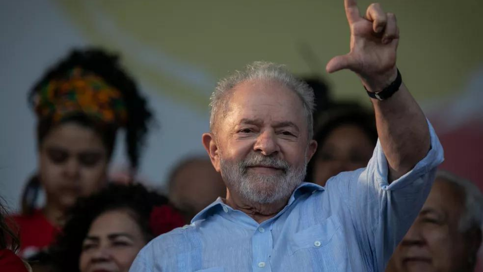 Presença de Lula no Rio atrai multidão. Foto de Lula fazendo o sinal de L com a mão e sorrindo.