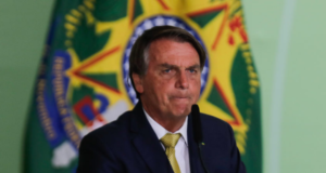 Bolsonaro conta a piada do dia: "Não tomamos decisões pensando nas eleições". Foto de Bolsonaro com expressão de preocupação falando ao microfone.