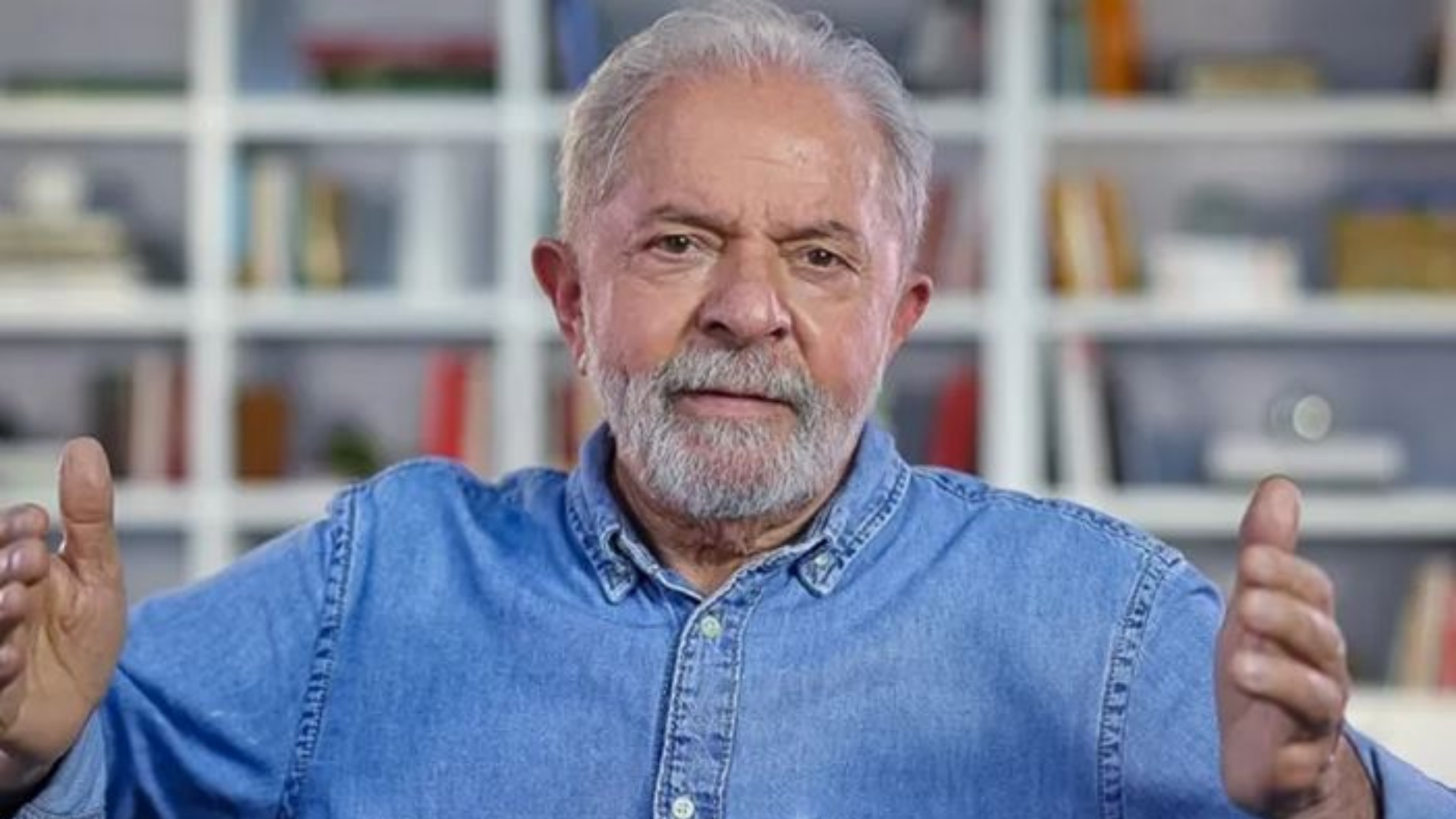 Lula teme assassinato por parte de bolsonaristas. Ele tem os braços levantados na altura do ombro, olhar sério e veste uma camisa jeans.