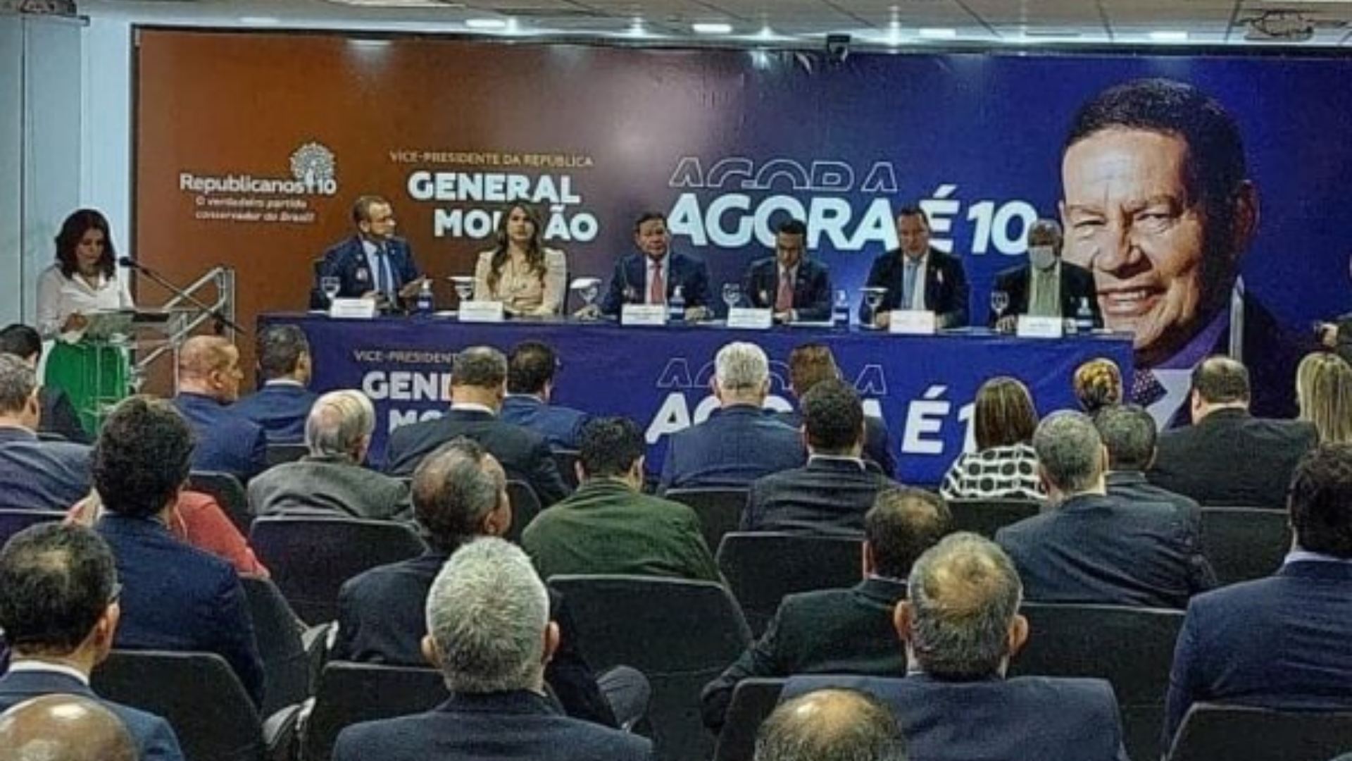 Militares fazem pouco caso de filiação de Mourão ao Republicanos. Foto do evento de filiação de Mourão, pessoas em um auditório com uma mesa e um banner com a imagem do vice-presidente.