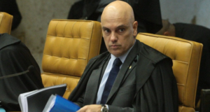 Moraes dá 24h para Telegram cumprir determinações pendentes. Foto do ministro com terno preto e bata do STF, com expressão séria.