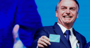 Bolsonaro gasta quase R$ 2 milhões com cartão corporativo em um mês. Foto de Bolsonaro sorrindo comum cartão na mão.