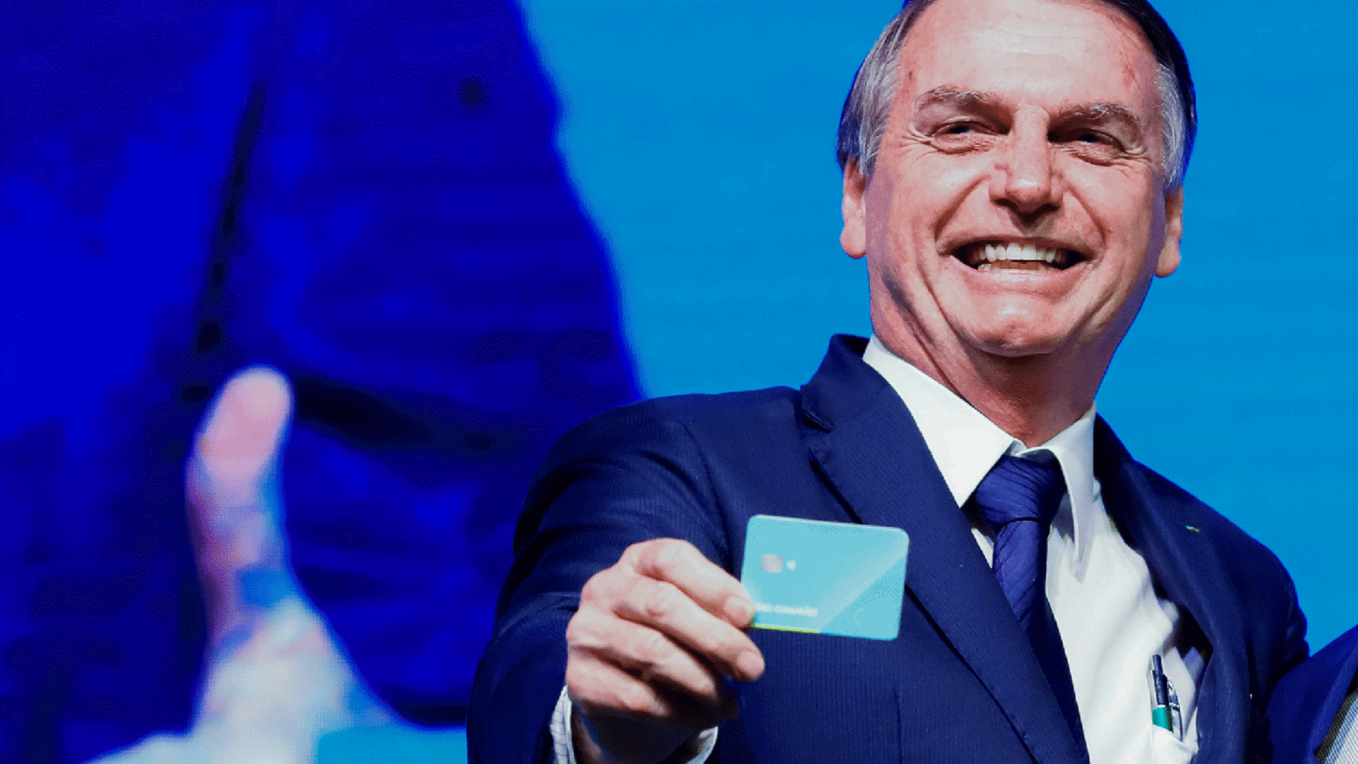 Bolsonaro gasta quase R$ 2 milhões com cartão corporativo em um mês. Foto de Bolsonaro sorrindo comum cartão na mão.