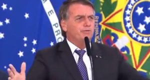 Bolsonaro faz discurso contra a vacina e grita: "Deixa eu morrer". Ele usa terno preto e está em púlpito falando ao microfone.