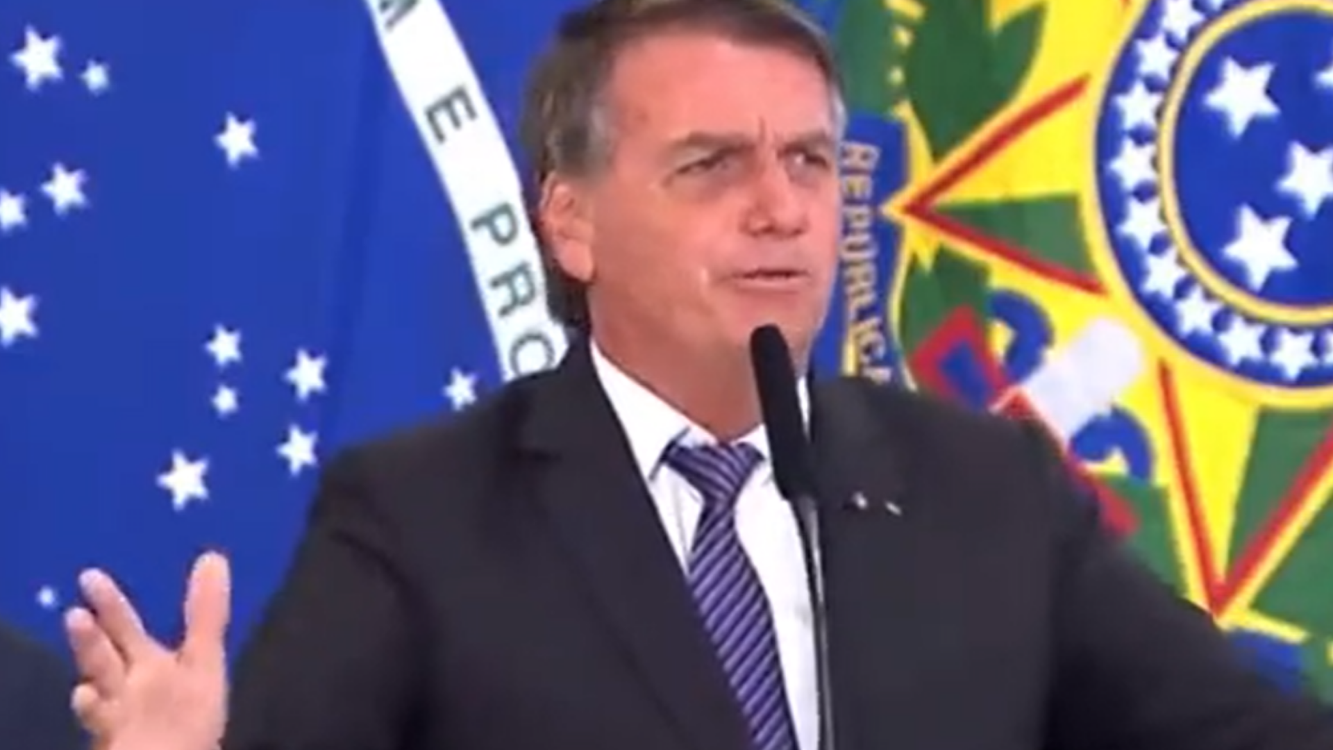 Bolsonaro faz discurso contra a vacina e grita: "Deixa eu morrer". Ele usa terno preto e está em púlpito falando ao microfone.