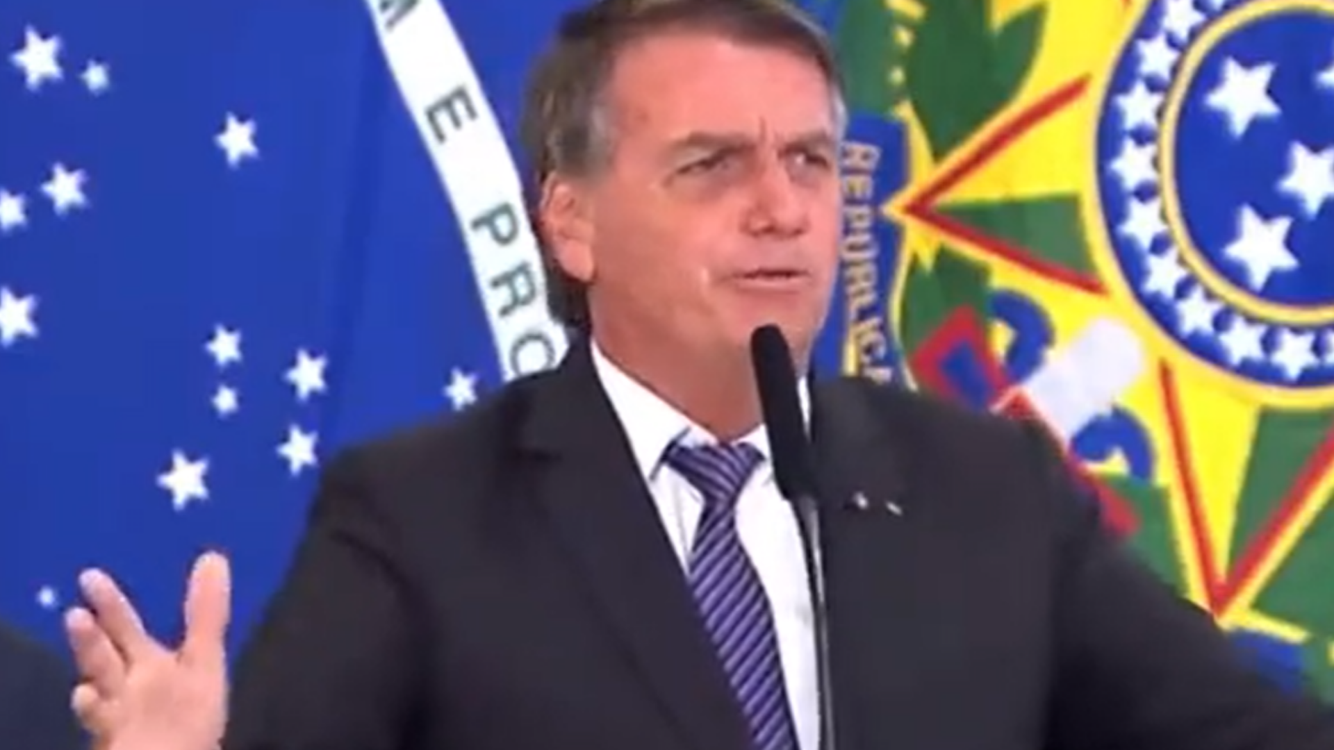 Bolsonaro faz discurso contra a vacina e grita: "Deixa eu morrer". Ele usa terno preto e está em púlpito falando ao microfone. 