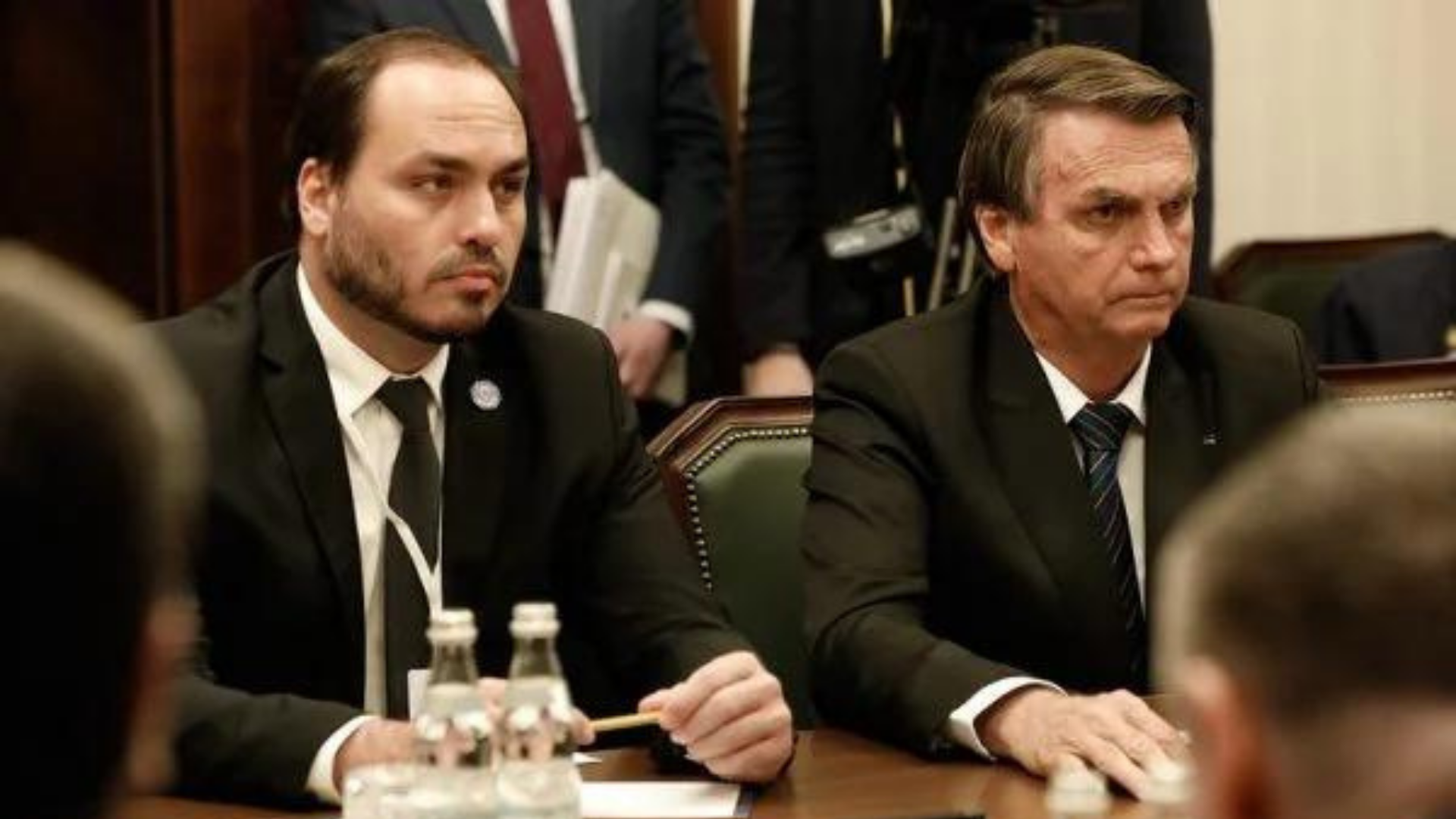 Viagem de Carlos Bolsonaro à Rússia preocupa STF e TSE. foto de Carlos Bolsonaro junto com o presidente em evento na Rússia. Ambos utilizam terno preto e estão sem máscara.