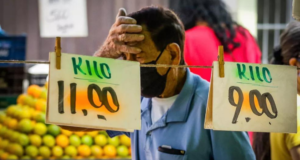 Quase metade do país espera cenário pior na economia, diz Datafolha. Foto d eum comerciante limpando o suor da testa, à frente, duas folhas de papel informando o preço dos alimentos.