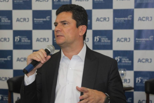 Foto de Sergio Moro, usando terno preto e falando ao microfone, durante um evento.