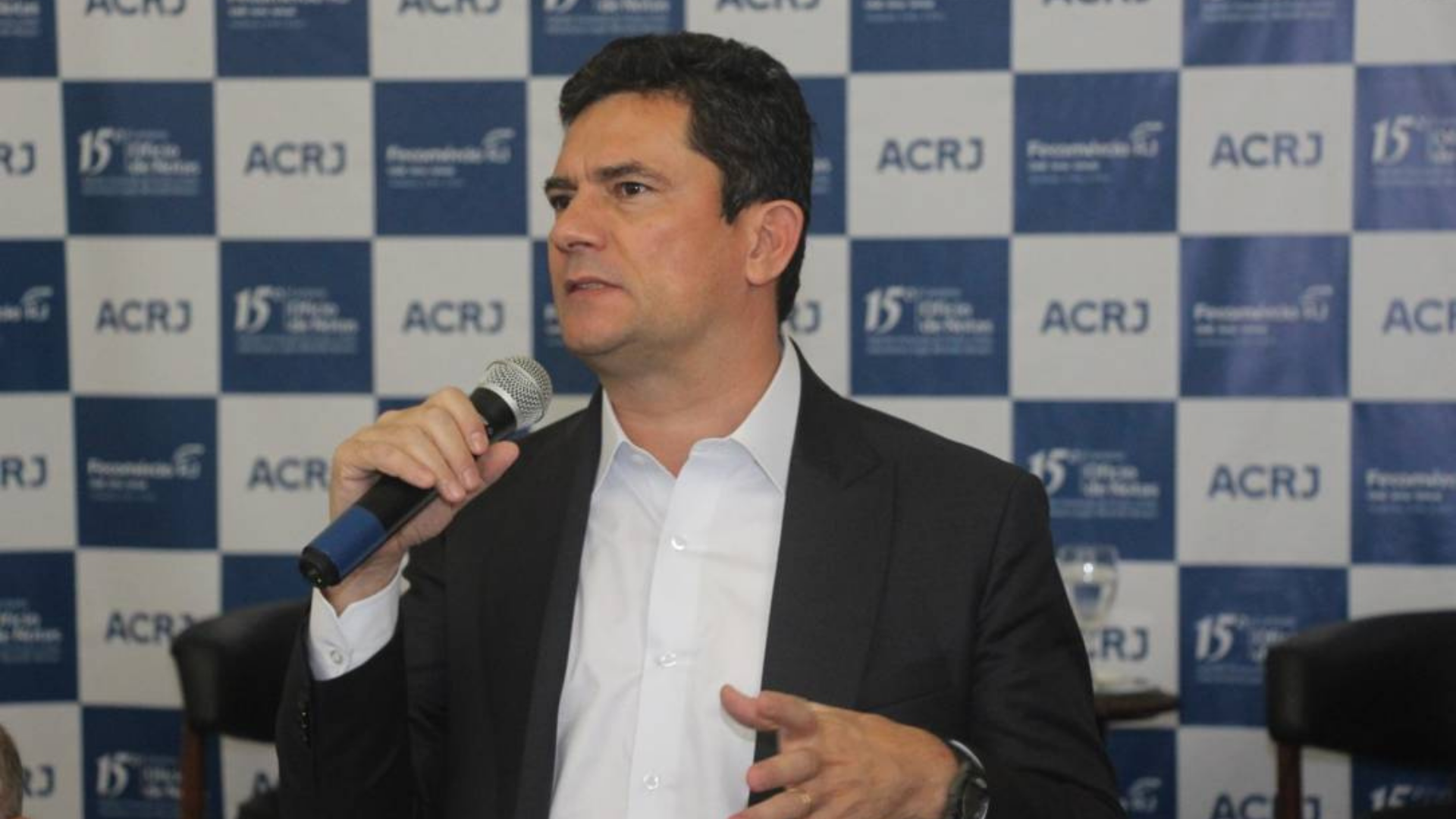 Foto de Sergio Moro, usando terno preto e falando ao microfone, durante um evento.