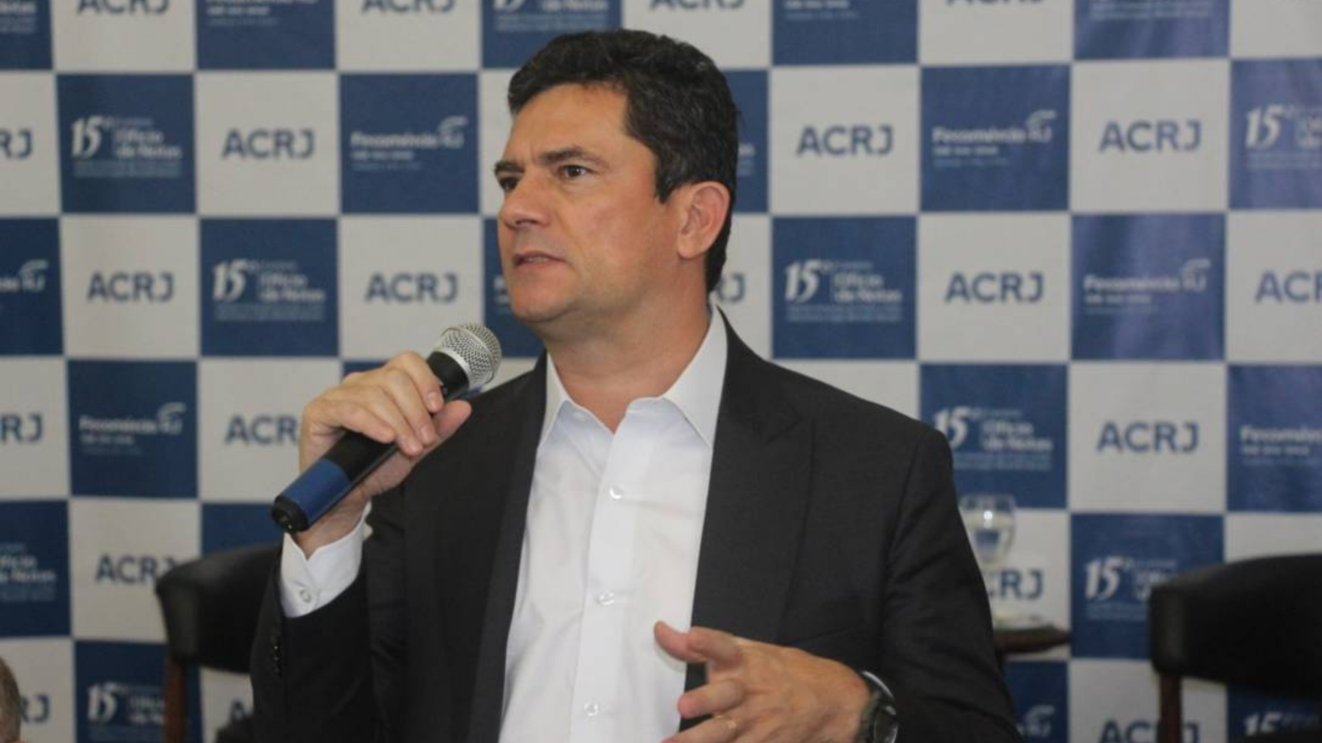 Hipocrisia? Moro critica Centrão, mas revela conversa com o União Brasil. Foto de Sergio Moro, usando terno preto e falando ao microfone, durante o evento. 