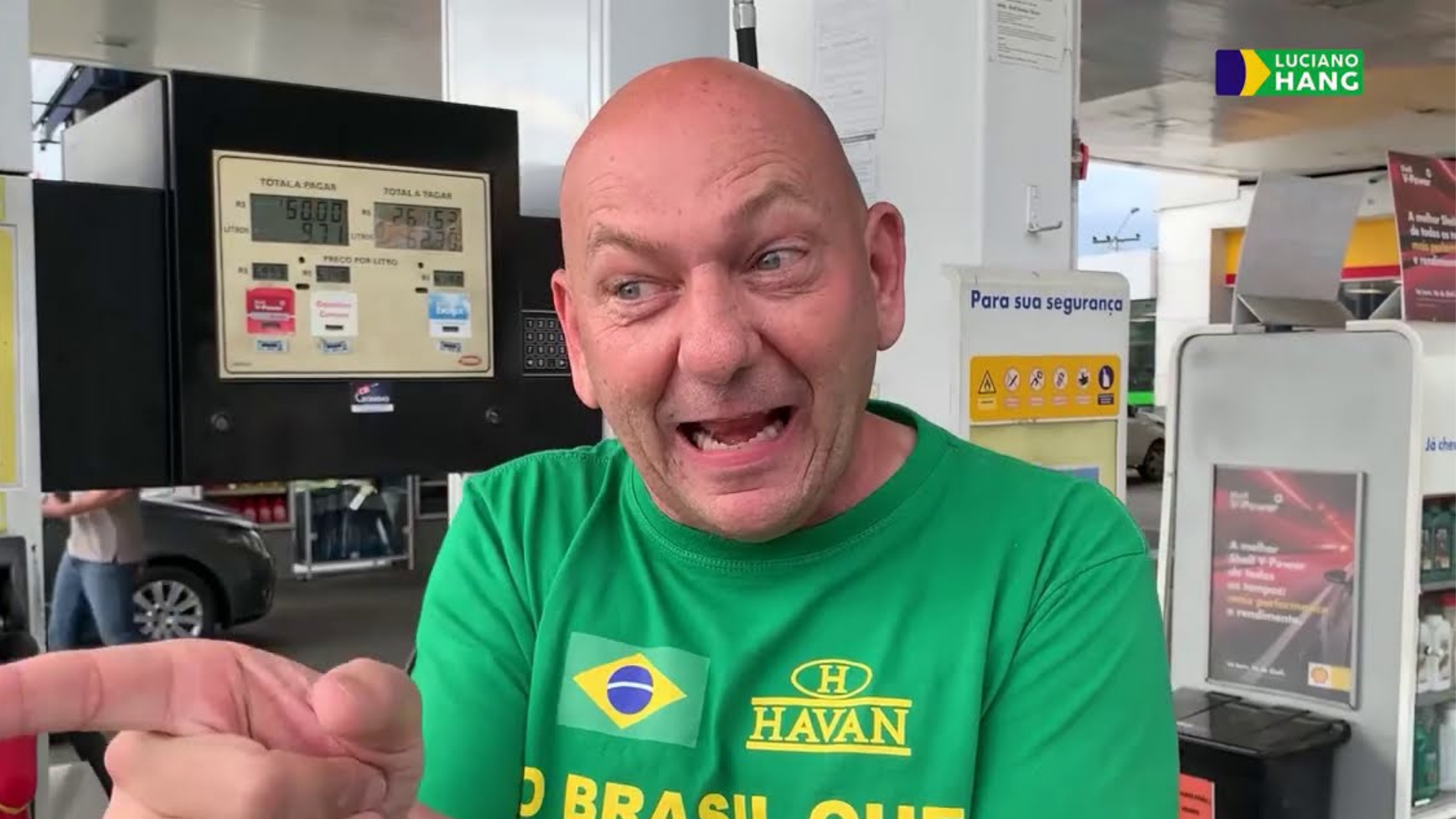 Luciano Hang distorce dados sobre governo Lula e mente. Foto de luciano Hang em um posto de combustível sorrindo e apontando o dedo indicador direito.
