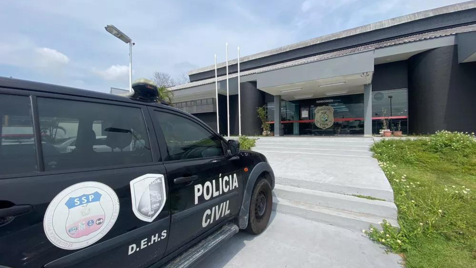 Polícia prende acusados de manter empresário em cativeiro na cidade de Manaus. Foto da sede da polícia junto com um carro ao lado.