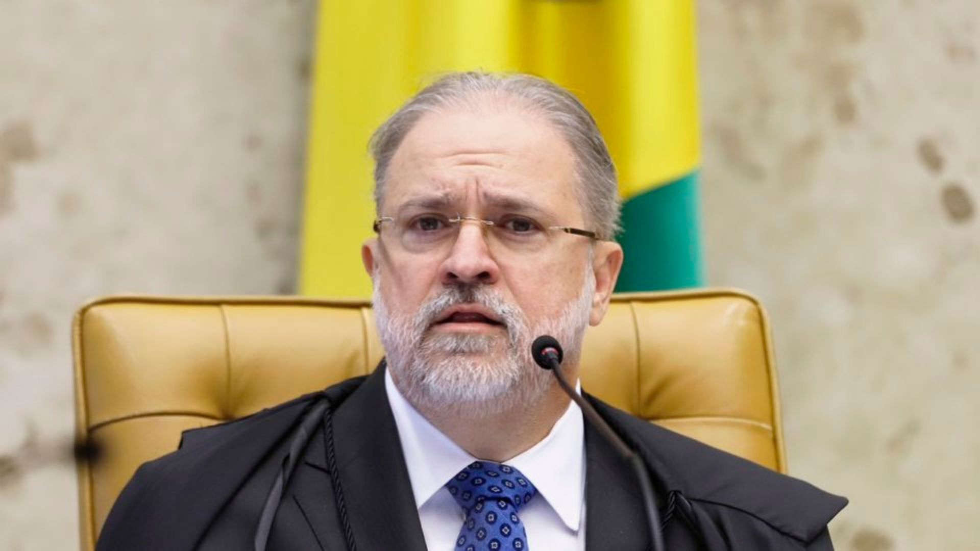 PGR pede arquivamento de processo que investiga Aras. O PGR aparece sentando em cadeira com expressão de preocupação, ele usa terno preto, barba branca e cabelo grisalho.