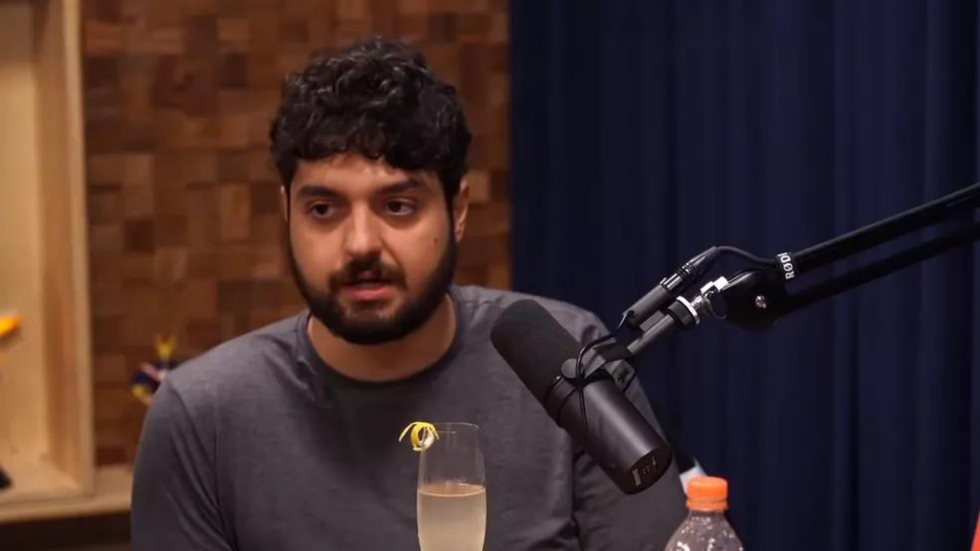 Monark e Ferréz migram para plataforma concorrente do YouTube. Foto de Monark falando ao microfone. Ele tem cabelos pretos e barba preta.