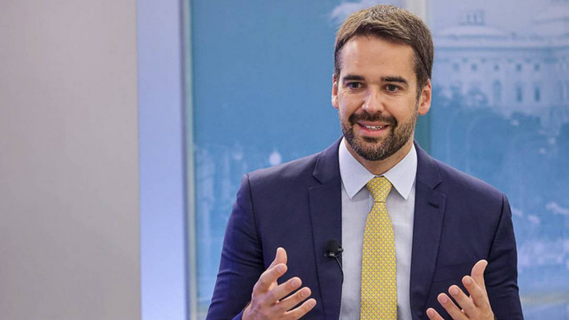 Eduardo Leite poderá ficar no PSDB, mas exige condições. Ele usa terno azul, gravata amarela, barba, olhar sério e mãos erguidas na altura do peito.