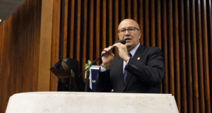 Luiz Claudio Romanelli usando terno preto, fala ao microfone em um púlpito, usa óculos e tem cabelo calvo.