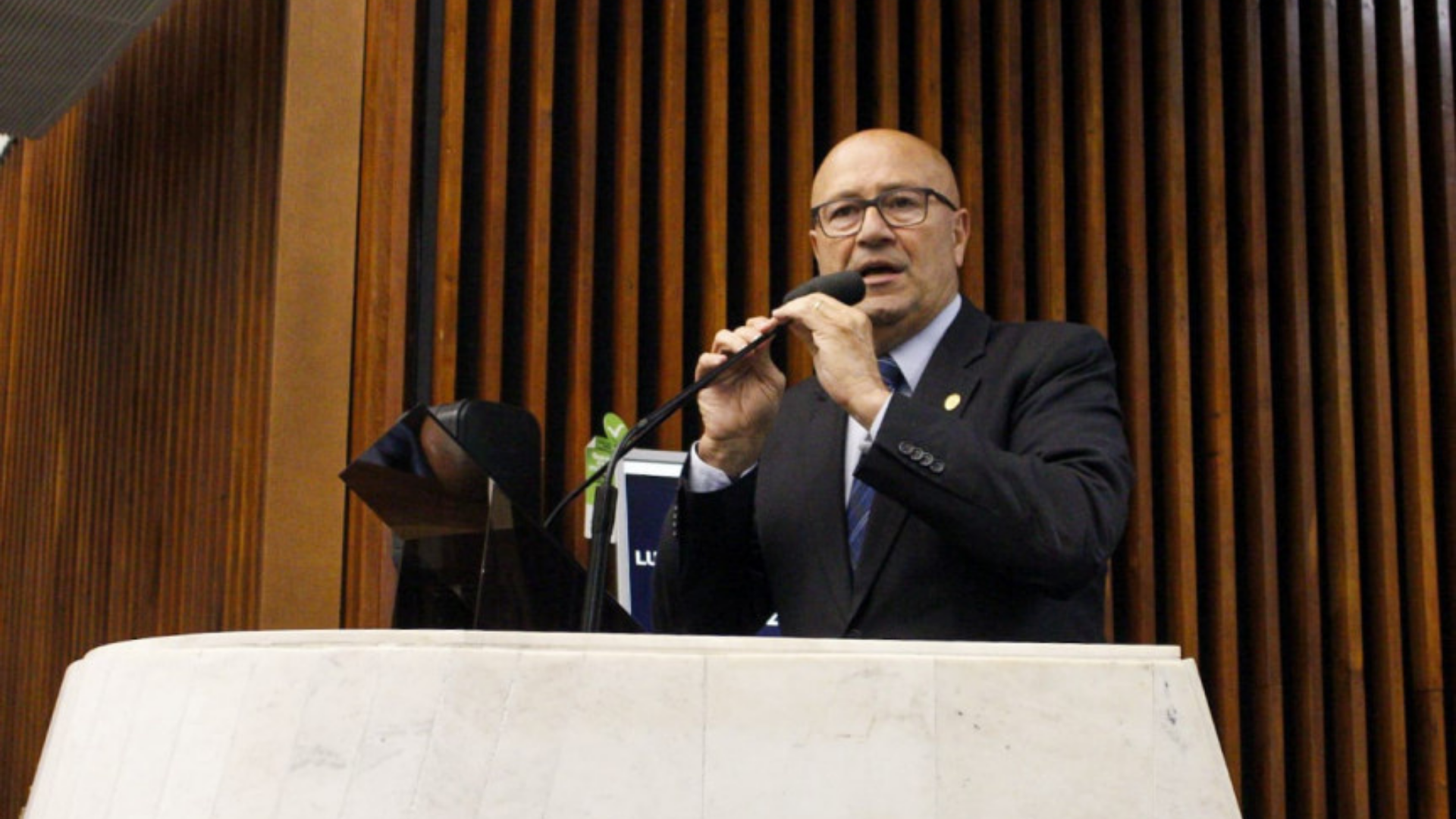 O fim da pandemia. Luiz Claudio Romanelli usando terno preto, fala ao microfone em um púlpito, usa óculos e tem cabelo calvo.