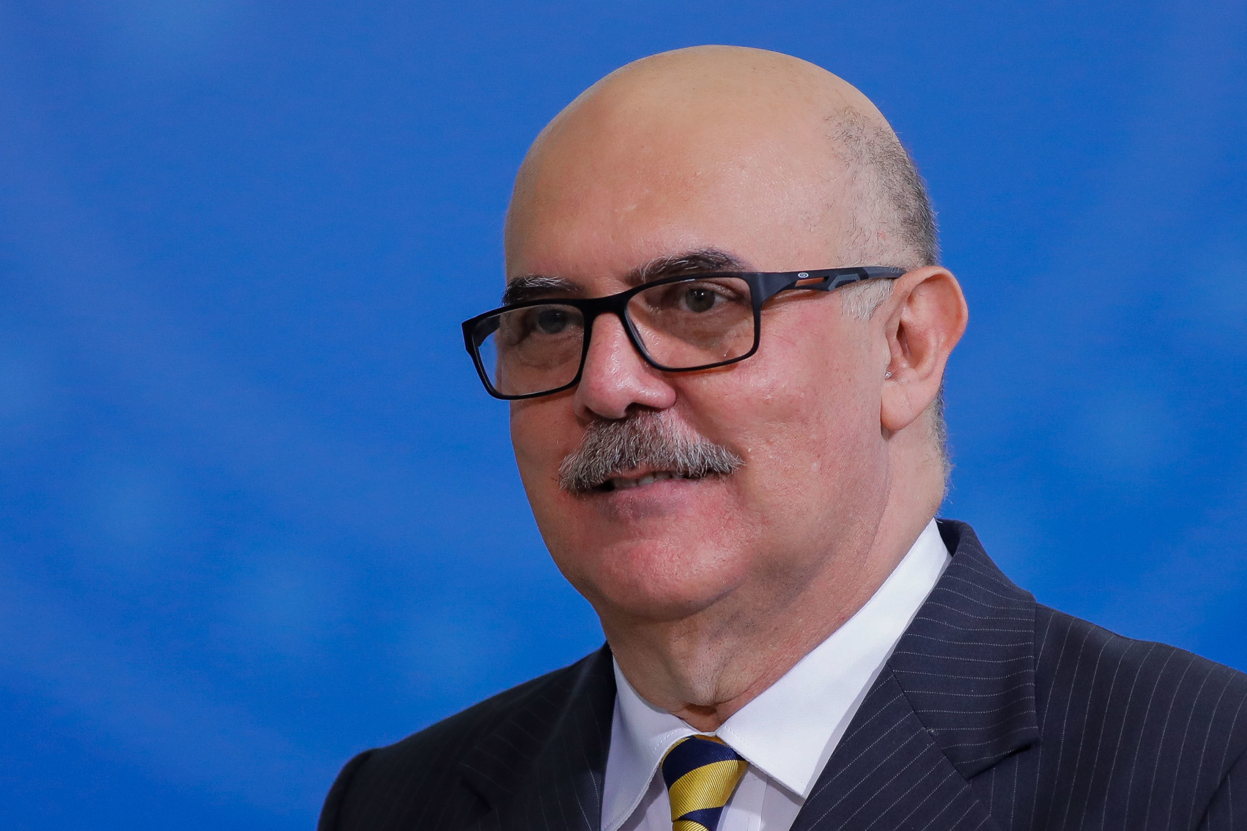 Foto do ministro Milton Ribeiro usando óculos e com fundo azul.