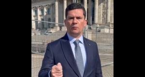 Sergio Moro, de terno, gravando vídeo na rua, na Alemanha. Ele gesticula com a mão fechada.