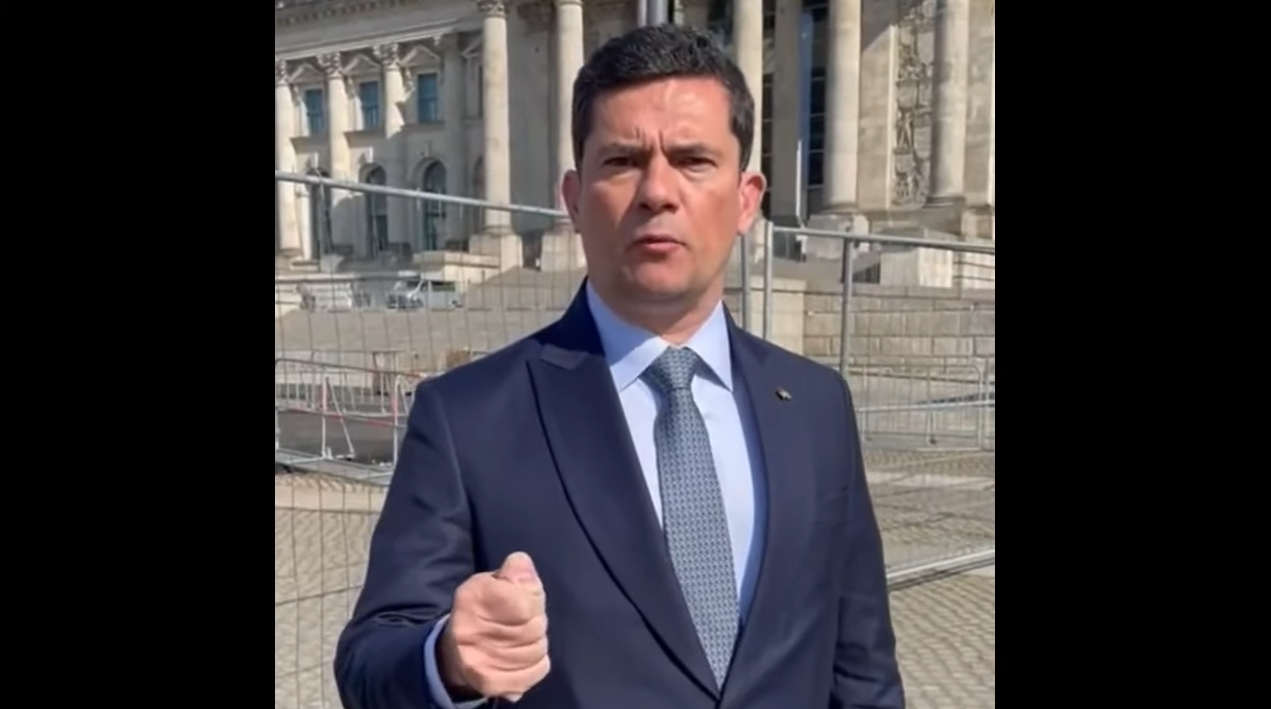 Sergio Moro, de terno, gravando vídeo na rua, na Alemanha. Ele gesticula com a mão fechada.