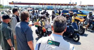 Bolsonaro e o ministro Tarcísio de Freitas, de costas, cumprimentando a motociata que passa em sua frente.