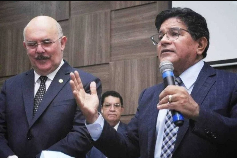 O ministro da Educação, Milton Ribeiro, ao lado do pastor Arilton Moura, que fala ao microfone. Ambos vestem terno e gravata.