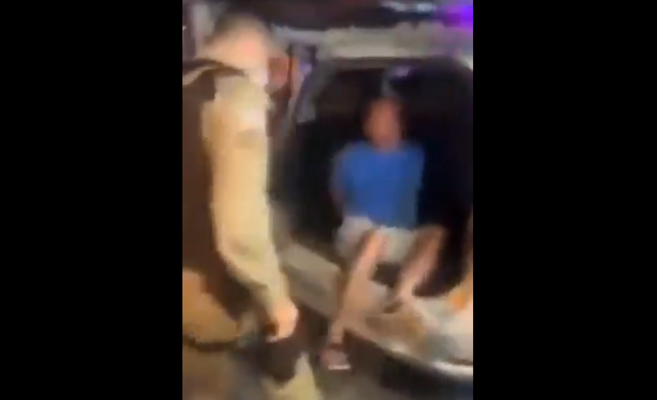 Homem sendo colocado no porta-malas da viatura por policiais em Porto Seguro