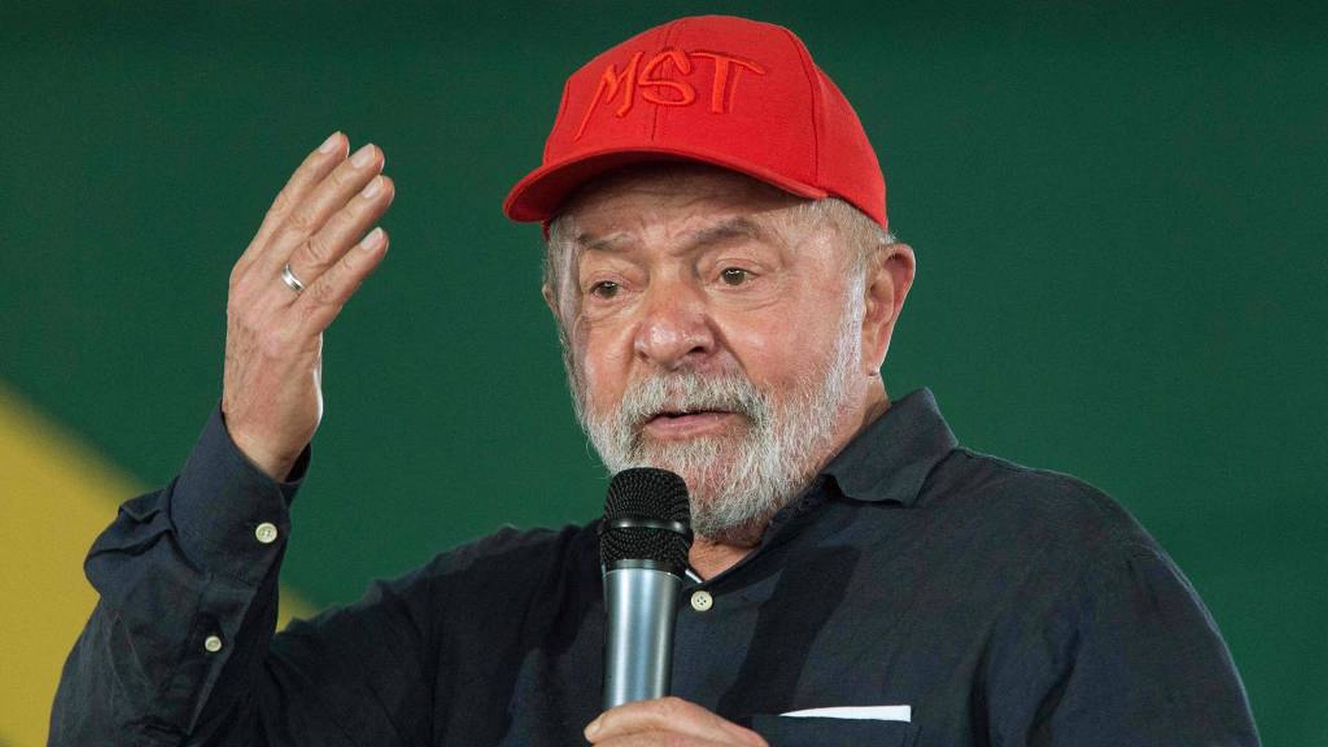 O ex-presidente Lula durante evento do PT. Ele usa um boné vermelho e fala ao microfone.