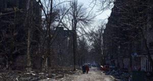 Moradores locais caminham perto de edifícios residenciais que foram danificados durante o conflito Ucrânia-Rússia na cidade portuária sitiada de Mariupol, Ucrânia, em 18 de março de 2022