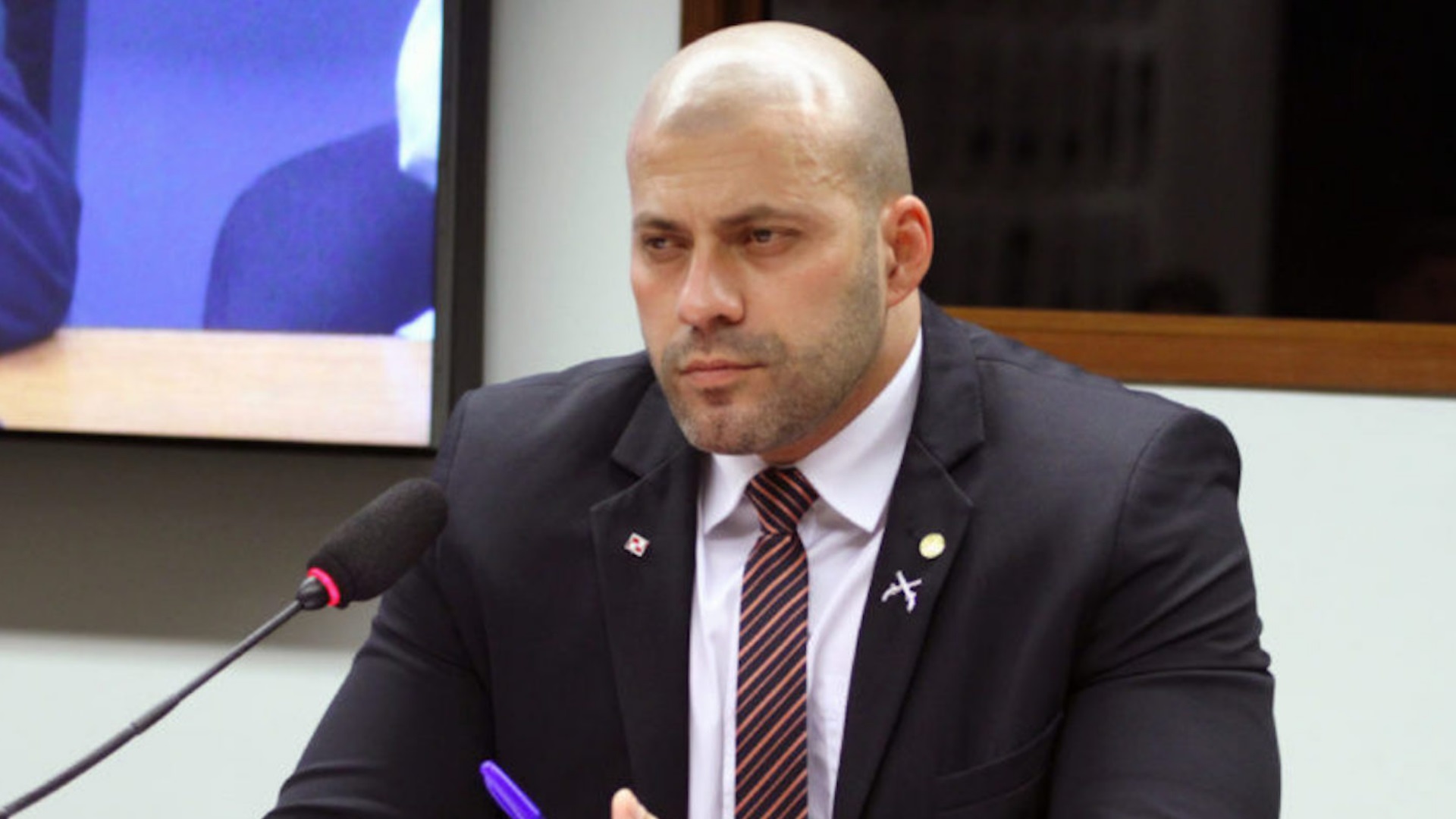 O deputado Daniel Silveira, com expressão séria e um microfone à sua frente, na Câmara dos Deputados.