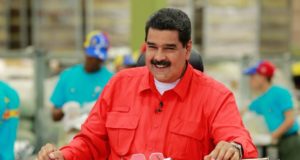 Nicolás Maduro sorrindo durante discurso. Ele veste uma camisa vermelha.