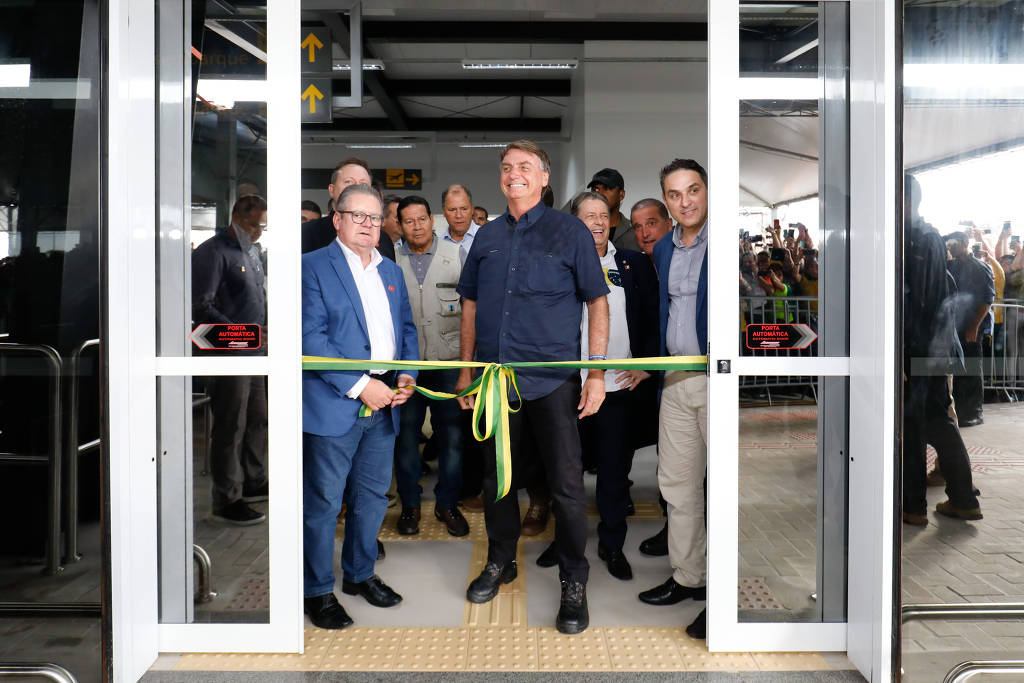 O presidente Jair Bolsonaro (PL) com outras autoridades na cerimônia de cortar a faixa de inauguração do aeroporto. Ele sorri para a foto.