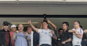 Bolsonaro em um camarote do estádio do Santos em 2019. Ele cumprimenta apoiadores com as mãos.